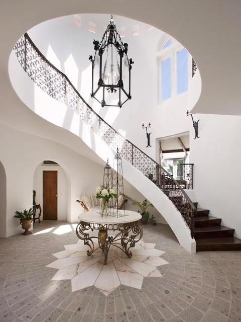 Foyer with two story iron railing stairs, a stone floor with a marble sunburst, a round table with iron work legs and Moroccan inspired iron pendant light