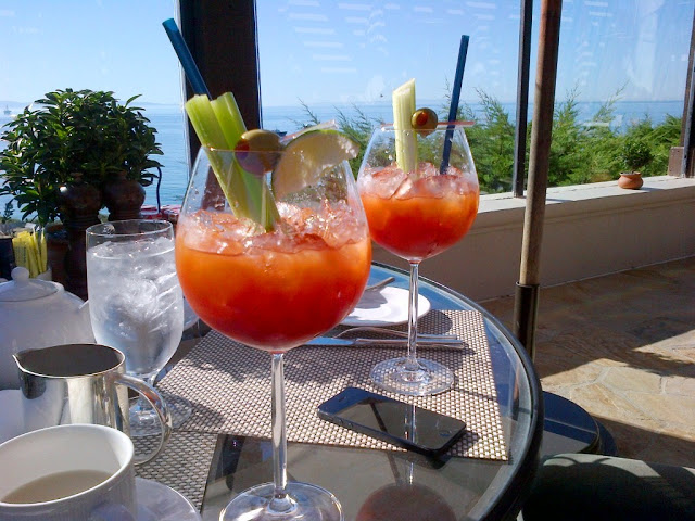 Bloody Mary's sitting on a glass table on a patio with an ocean view