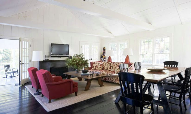 family room with trestle dining table, red sofa chairs, sisal rug, wall mounted television, vaulted ceiling beams, a fire place, french doors and a patterned sofa