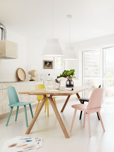 bright dining room with wood table, mismatched pastel and colored chairs, wood cabinets and white pendant lights