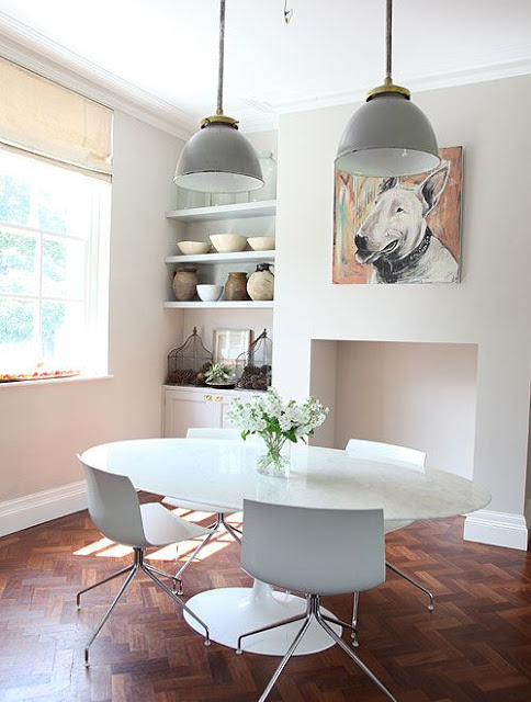 breakfast nook in a country house in the UK with white tables and chairs, a painting of a bull terrier hanging over what was once a fireplace, gray walls, and walnut herringbone wood floors