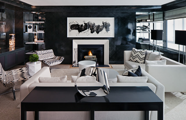 haus' interior living room with black lacquer wall paint, chevron pillows and upholstered lounge chairs, white sofas, fireplace with modern art hanging on the wall above it