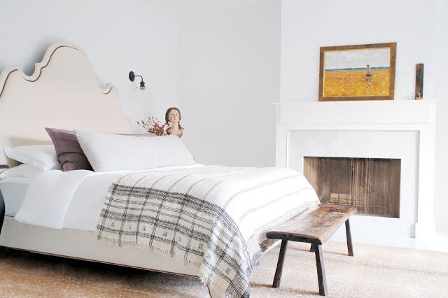 bedroom with upholstered headboard, fireplace and reclaimed wood bench at the foot of the bed