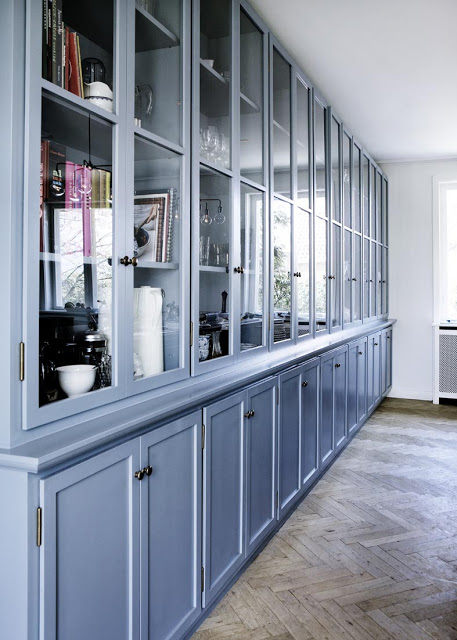 close up of cabinets with glass panes in a blue kitchen with herringbone wood floors