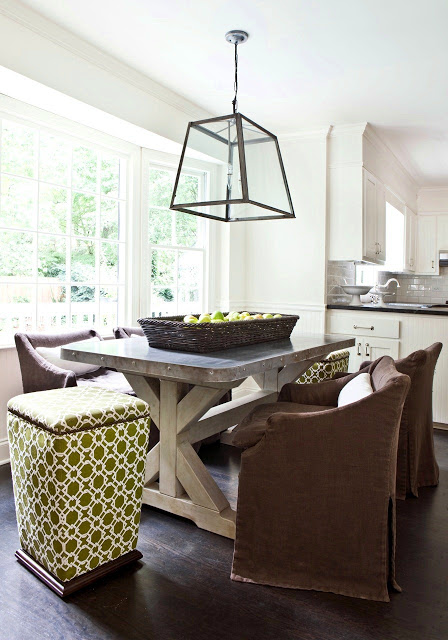 Breakfast nook with a trestle table, metal top, low back upholstered chairs, green graphic patterned stools, and a large brass and glass pendant light