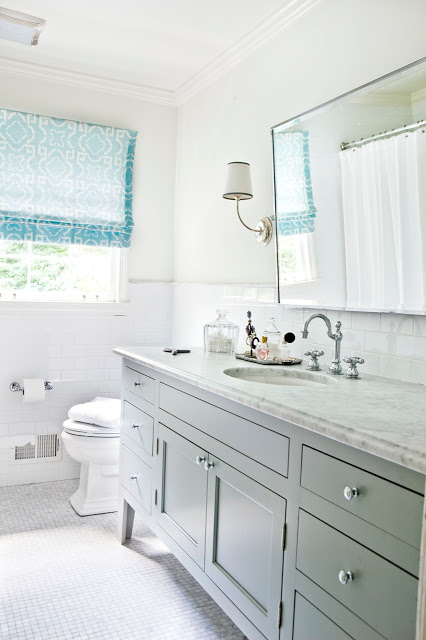 White bathroom with light blue Roman shades, marble counters, hexagon mosaic tile floor and a large mirror