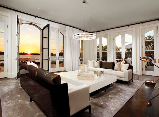 living room in an waterfront home on Harbor Island, in Newport Beach with an ocean view, french doors, dark wood floors, dueling modern white and brown sofas, white floor length curtains, a large square coffee table, and a small chandelier