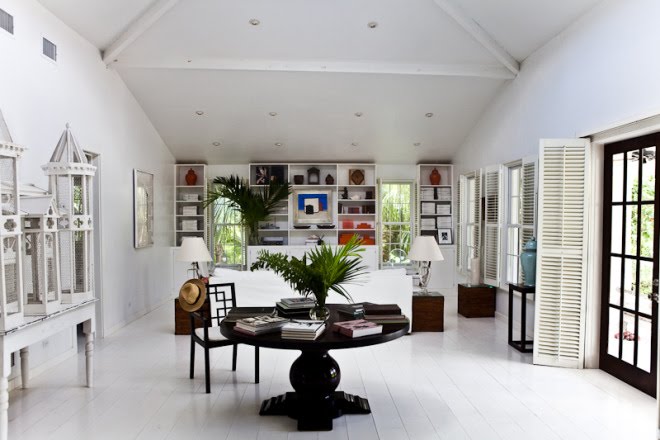 White living room with painted wood floor, exposed beams, white built in bookshelves, Moroccan lanterns, and a round dark wood table and chair