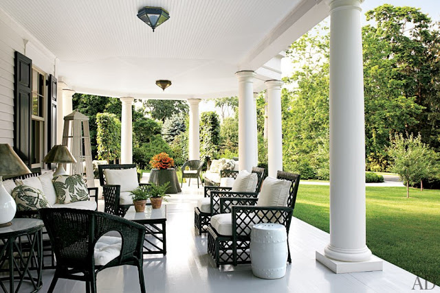 Black and white patio with black wicker furniture with white cushions, antique rattan chairs also with white cushions overlooking a lawn with small trees