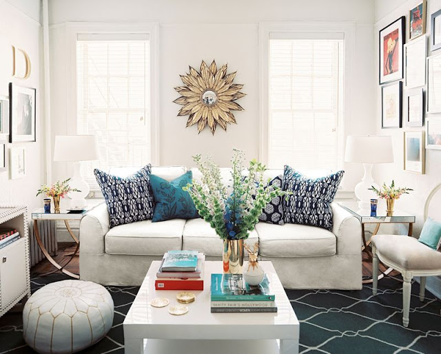 Living room with white sofa, navy fence print rug, a white coffee table, a white Moroccan pouf, large windows and a mirror in the shape of a sun