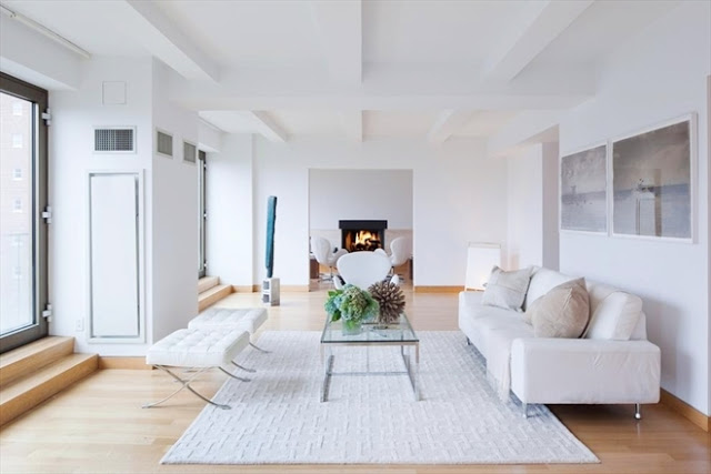 living room in a New York City penthouse apartment designed by John Pawson with light wood floors, a white rug, glass coffee table,white walls and white sofa