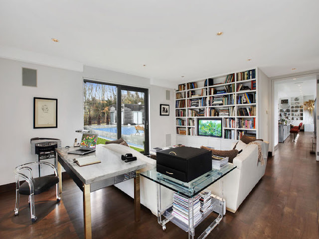 den in the Hamptons with wall sized book shelf, white sofas, wood floors and a glass coffee table