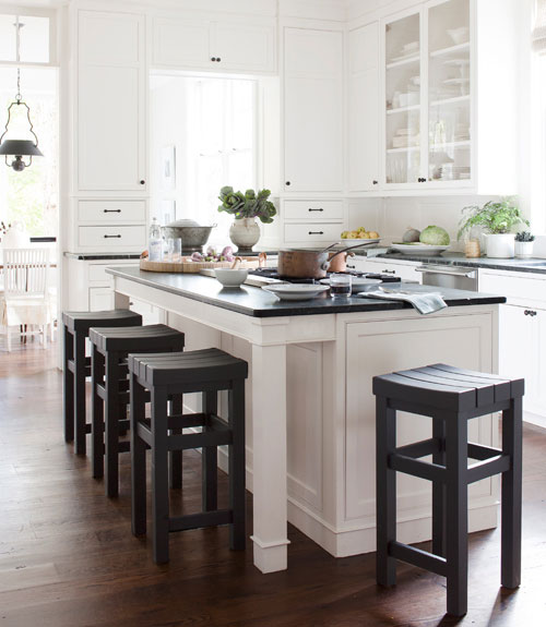 Kitchen with white cabinetry, dark green soapstone counters with a matching island and dark wood stools