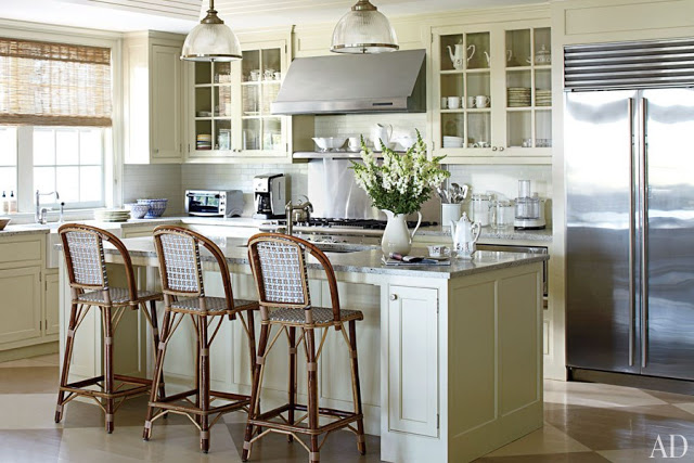 kitchen in Nantucket with stainless appliances, island with marble counter top and high chairs, two pendant lights, white cabinets and subway tile backsplash