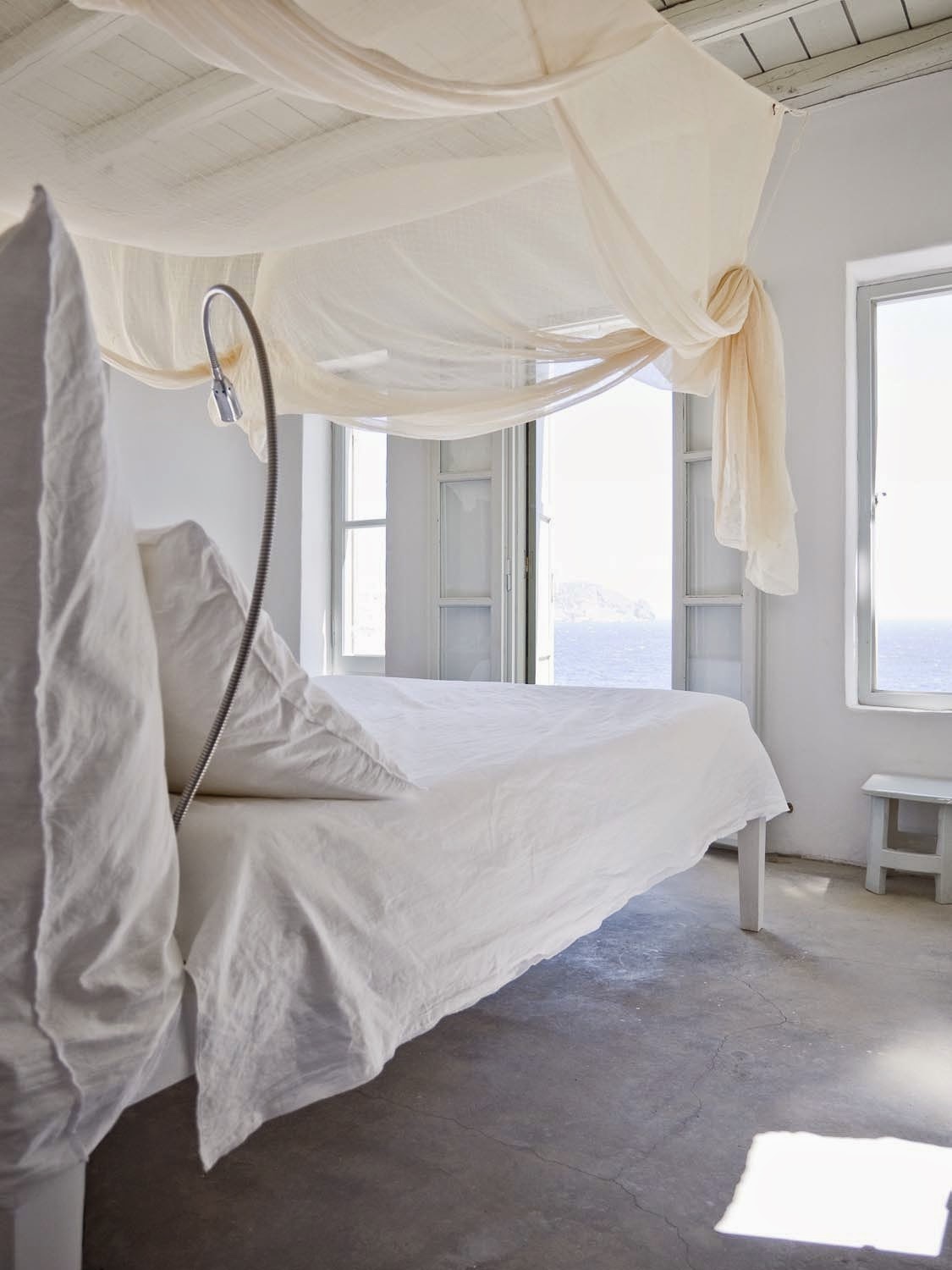 White bedroom with a canopy bed and ocean view by Jerome Galland