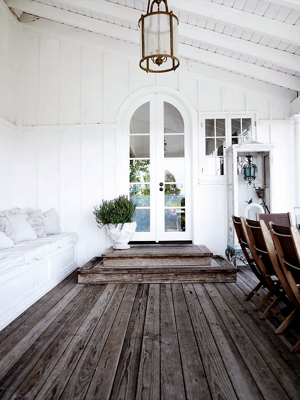 White arched doorway from a covered patio into a home with grey deck flooring and built in bench seating