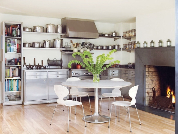 super small kitchen with stainless steel bottom cabinets and floating shelves, a circle table surrounded by white chairs and a fireplace