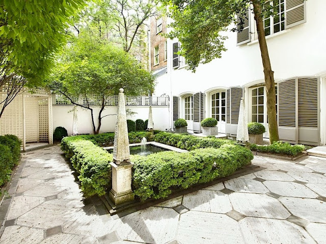 Exterior of a NYC townhouse with grey shutters and a manicured garden