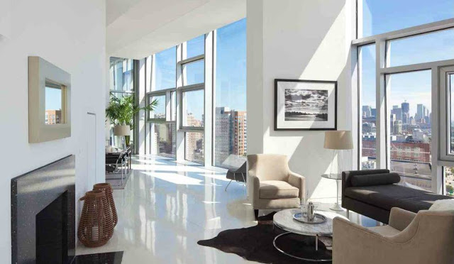 Den with encasement windows with amazing views of NYC, a fireplace, brown bench seating, cream armchairs and a round coffee table. 