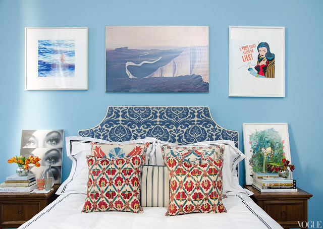 master bedroom with blue walls covered in art, upholstered ikat headboard, and ikat accent pillows