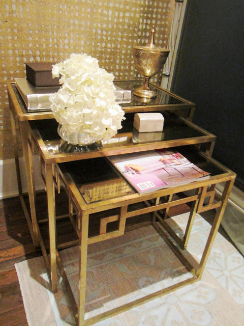 Three gold art-deco inspired nesting tables with a magazine, flower arrangement, wood box and a photo album in the Windsor house
