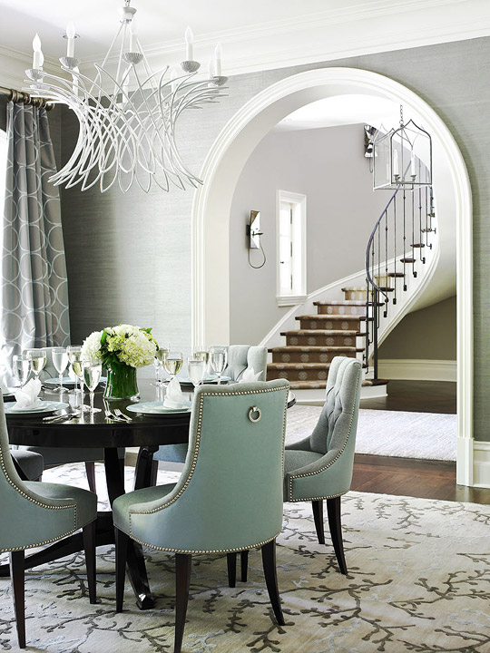 Dining room with arched entry way, wood floor, white chandelier, round, dark wood table surrounded by turquoise armchairs with nail head trim