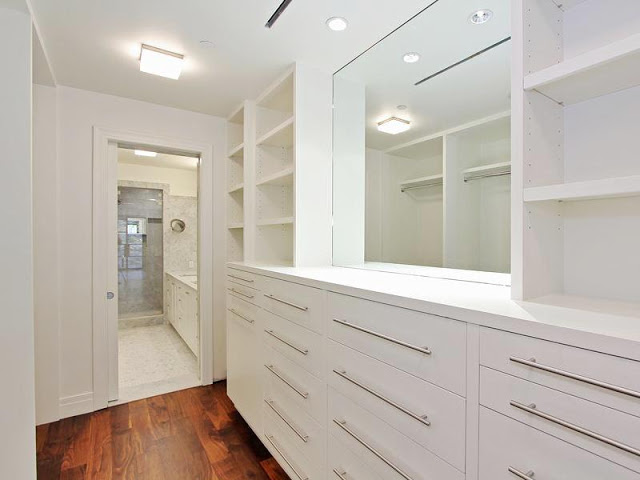 Walk in closet/dressing room with white cabinets and drawers with long silver drawer pulls and a wood floor