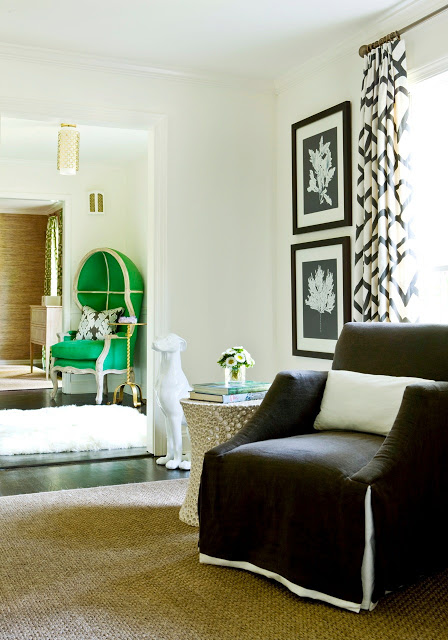 View from den to living room with a green dome chair, graphic black and white curtains, a dark brown armchair and a a woven sea grass sisal rug