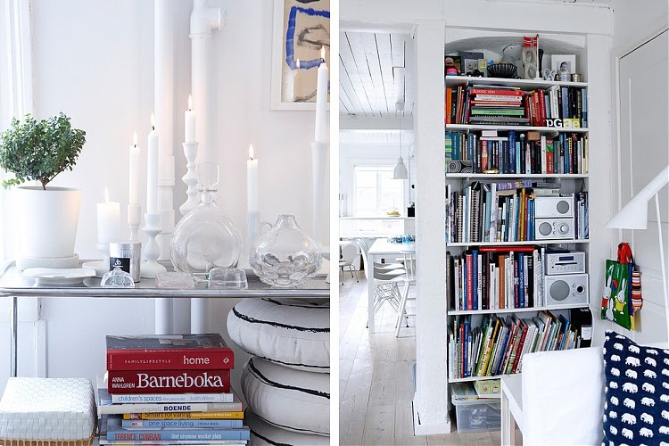 On the left is a close up of a table holding glass bottles and white candles in white candlesticks and a small plant in a white pot, on the right is a close up of a white built in shelf stuffed full of brightly colored books