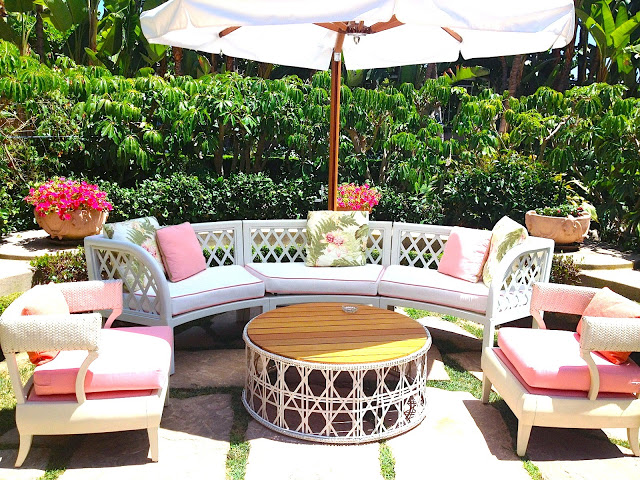 Outdoor sitting area white outdoor lounge chair with white cushions with pink piping round woven coffee table umbrella
