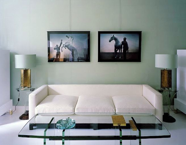 Den with sea foam walls, white sofa, glass coffee table and two pictures of a man with horses above the sofa