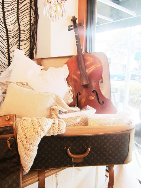 display in Pom Pom with their throws, pillow and a violin in a Louis Vuitton suitcase