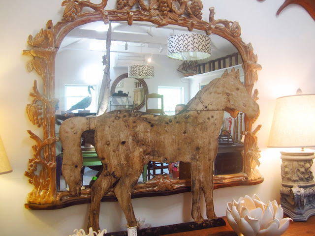 wood horse sculpture on a table leaning up against a large, gold trimmed mirror