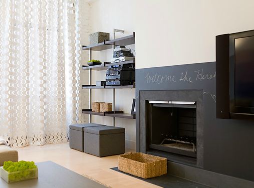 Den with white walls, floating shelves and a fireplace with the fireplace surround painted with chalkboard paint
