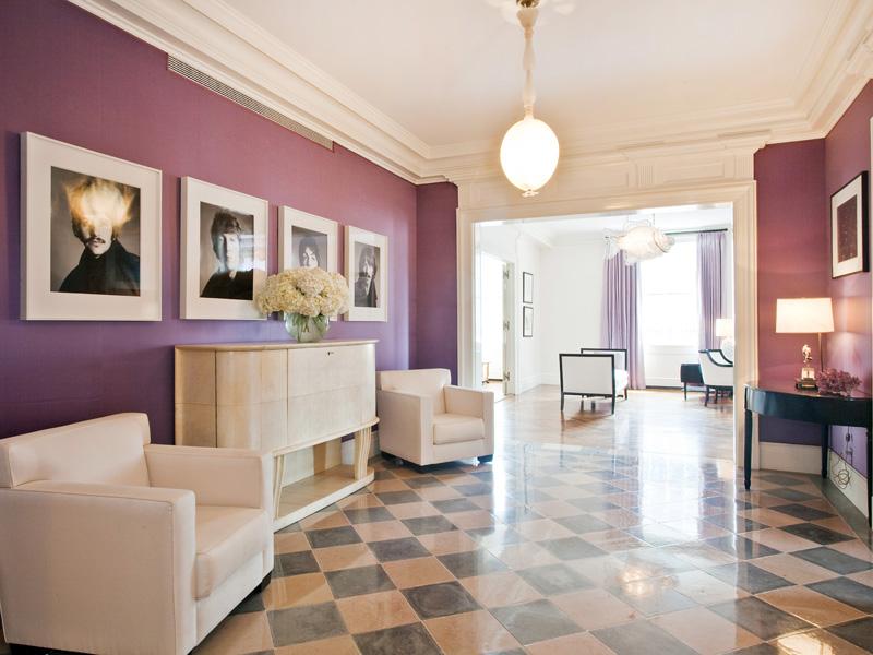Foyer in a purple park avenue apartment with a checkered marble floor, coffered ceiling, pendant light, white armchairs and a white chest of drawers