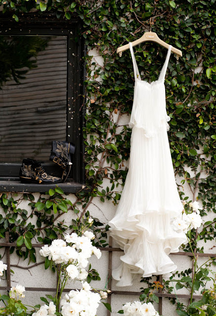 white Chloe gown hangs on a trellis of roses in a garden