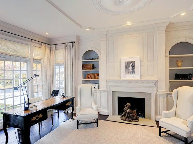 White study with writing desk, arched built in bookshelves shelves, a large window and dark wood floors