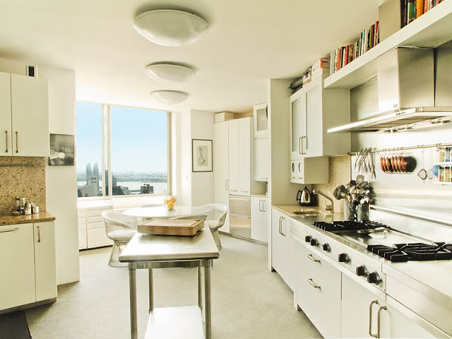 open kitchen with white cabinets and granite counter tops, and metal island. The hood is very flat and goes straight up into a floating bookshelf