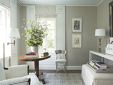 Alternate view of the grey bedroom where you can see a round wood table, a silver chair, a white armchair, a white ottoman holding a tray full of books and a long, white accent table