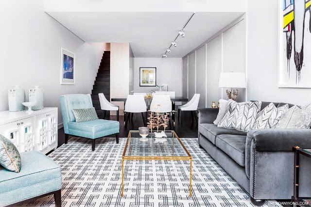 Bright living room in a Sydney loft with a geometric rug, grey sofa with nail head trim, turquoise chairs, a long white side table, and a glass coffee table with gold trim