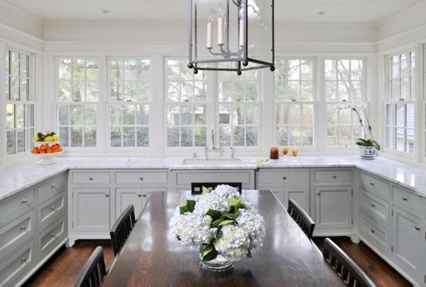 Kitchen with grey cabinets, marble counter tops, casement windows, stained oak table dining room table surrounded by matching chairs and a chandelier