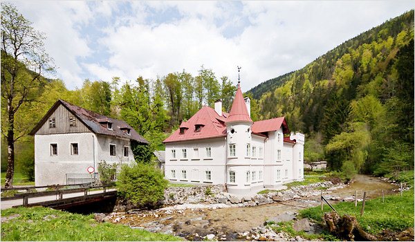 Alternate exterior view of The Hammerhaus castle with a view of trees, a large creek, and a bridge surrounding it