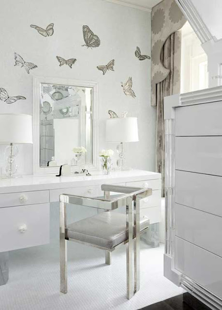Girly walk in closet with buttery fly wall paper, a vanity, large mirror, stainless chair and white cabinets