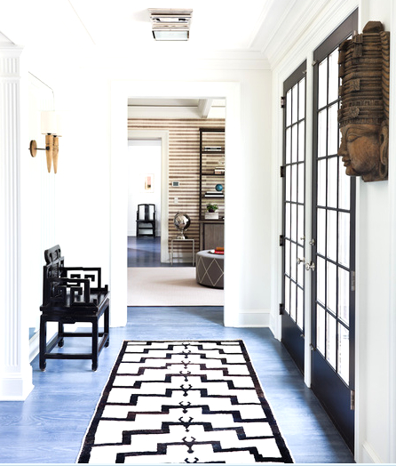 Hallway with blue stained wood floors, black paneled doors and a black chair with geometric arms