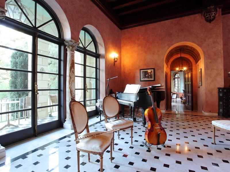 Music room in a Florentine style vila with two Louis XIV chairs, a cello, grand piano, black and white tile floor, arched entry ways, pink walls and exposed beams