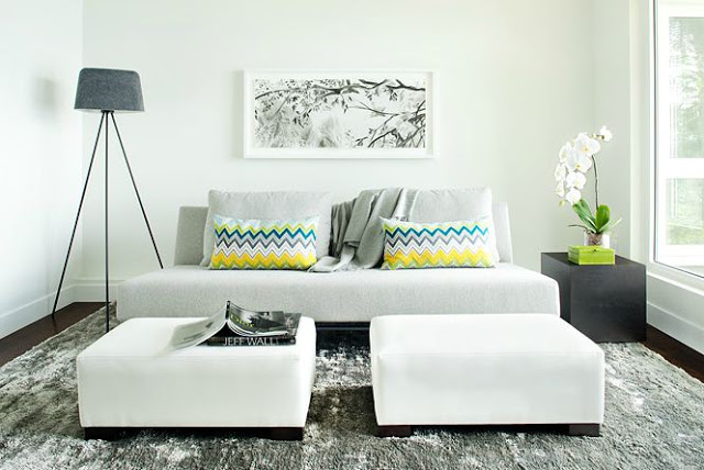 Modern living room with grey sofa with two matching ottomans, dark wood floors, accent pillows with Missoni-esque zig zag pattern in yellow, green, grey and white, a block side table and a modern style lamp