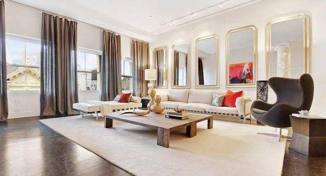 living room in a Soho Condo in New York with white sofa, gray table, decorative mirrors, gray floor length curtains, and orange accents