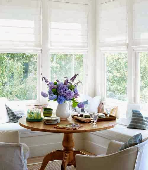 Bright breakfast nook with white roman shades, L-shaped banquette seating and a wood table