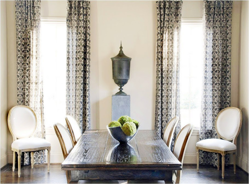 Dining room with high ceilings, classic chairs, long wood table, black urn, dark wood floor and printed curtains