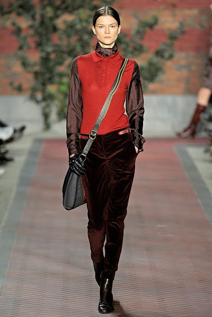 model from tommy hilfiger's fall 2012 runway show wearing rust velvet pants,a red vest with a peter pan collar and shiny brown long sleeve shirt holding an across the body bag